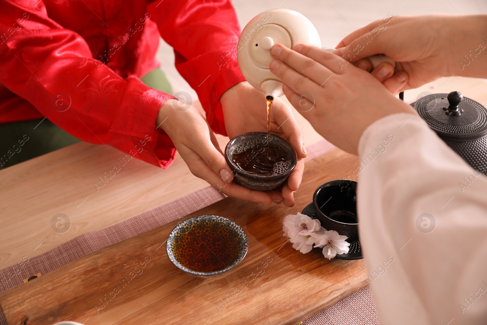 Photo of Master pouring freshly brewed tea into guest's cup during traditional ceremony at table, closeup