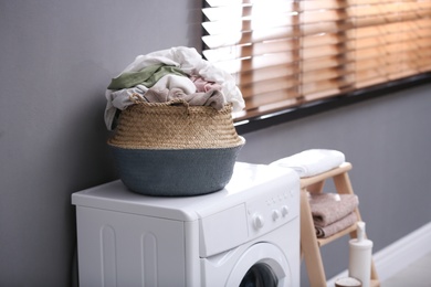 Wicker basket with dirty laundry on washing machine near grey wall indoors