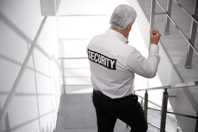 Photo of Professional security guard with flashlight on stairs indoors