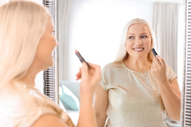 Photo of Mature woman applying makeup near mirror at home