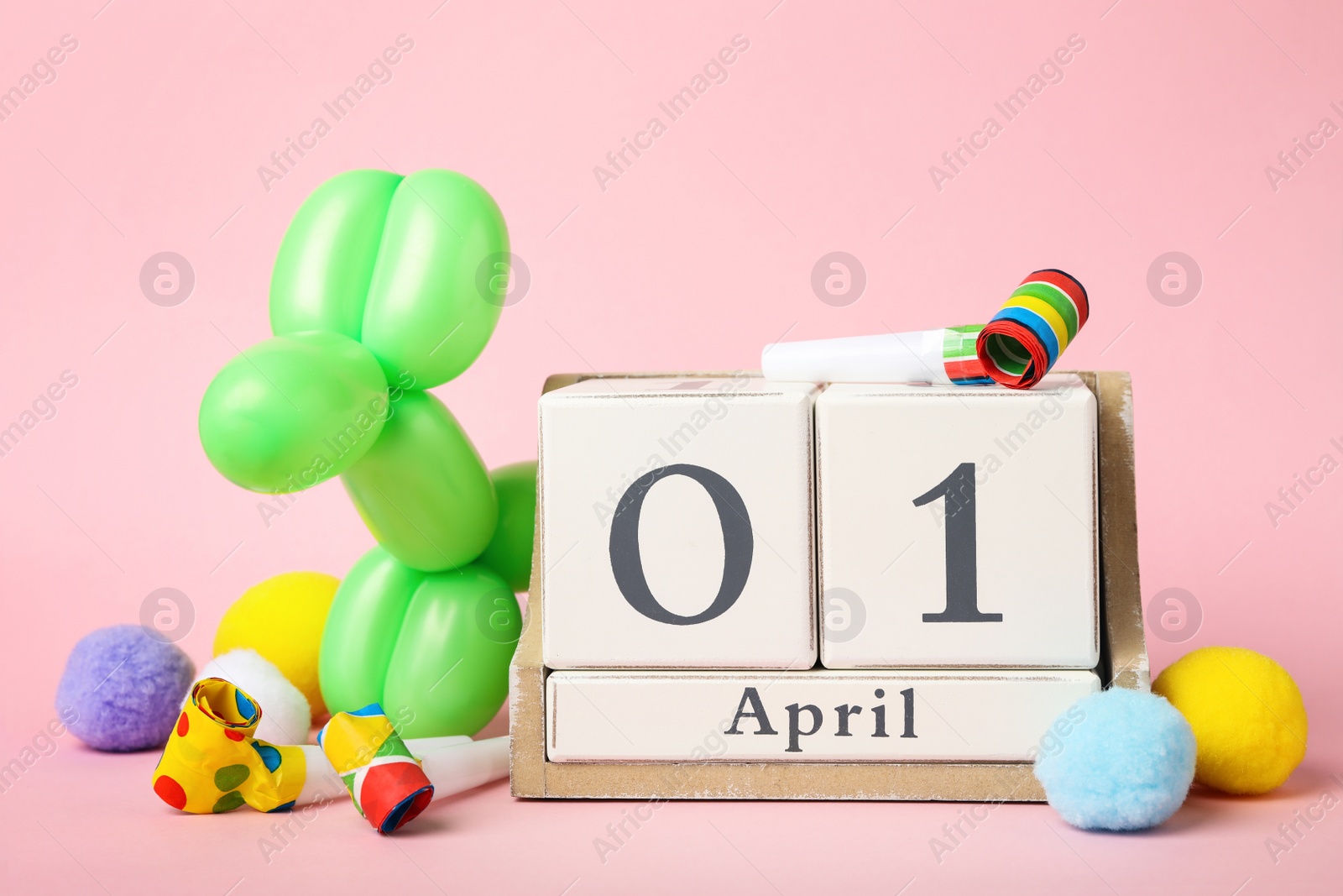 Photo of Wooden block calendar and party decor on pink background. April fool's day