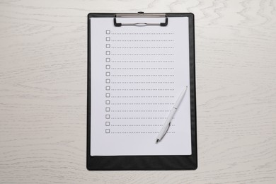 Photo of Clipboard with checkboxes and pen on wooden table, top view