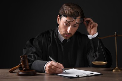 Emotional judge working with papers at wooden table against black background