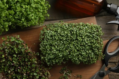 Photo of Fresh microgreens, spray bottle and scissors on wooden table, flat lay