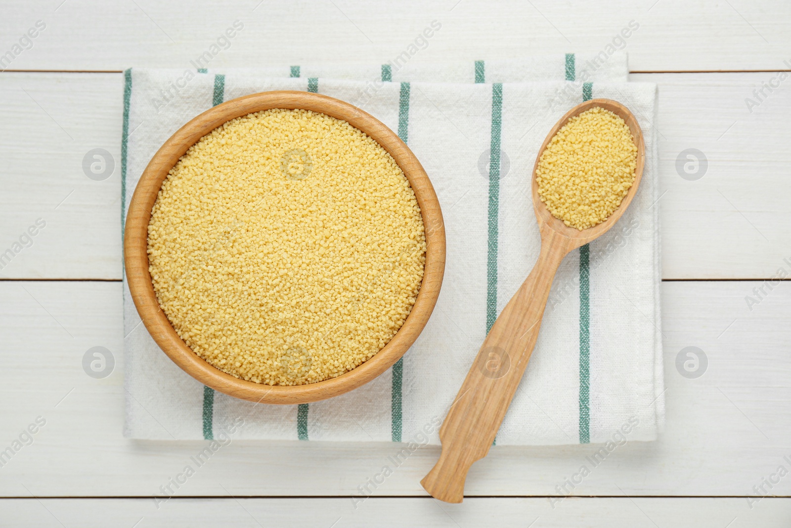 Photo of Bowl and spoon with raw couscous on white wooden table, top view