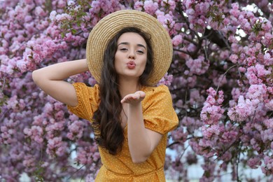 Beautiful woman blowing kiss near blossoming sakura tree on spring day