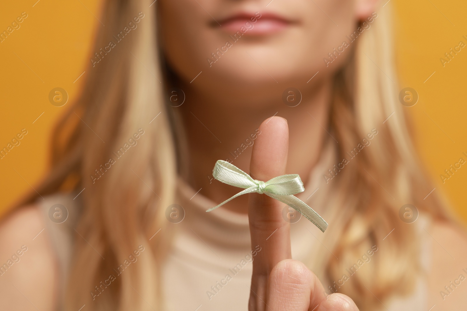 Photo of Woman showing index finger with tied bow as reminder against orange background, focus on hand