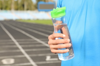 Photo of Sporty man holding bottle of water at stadium on sunny day, closeup. Space for text