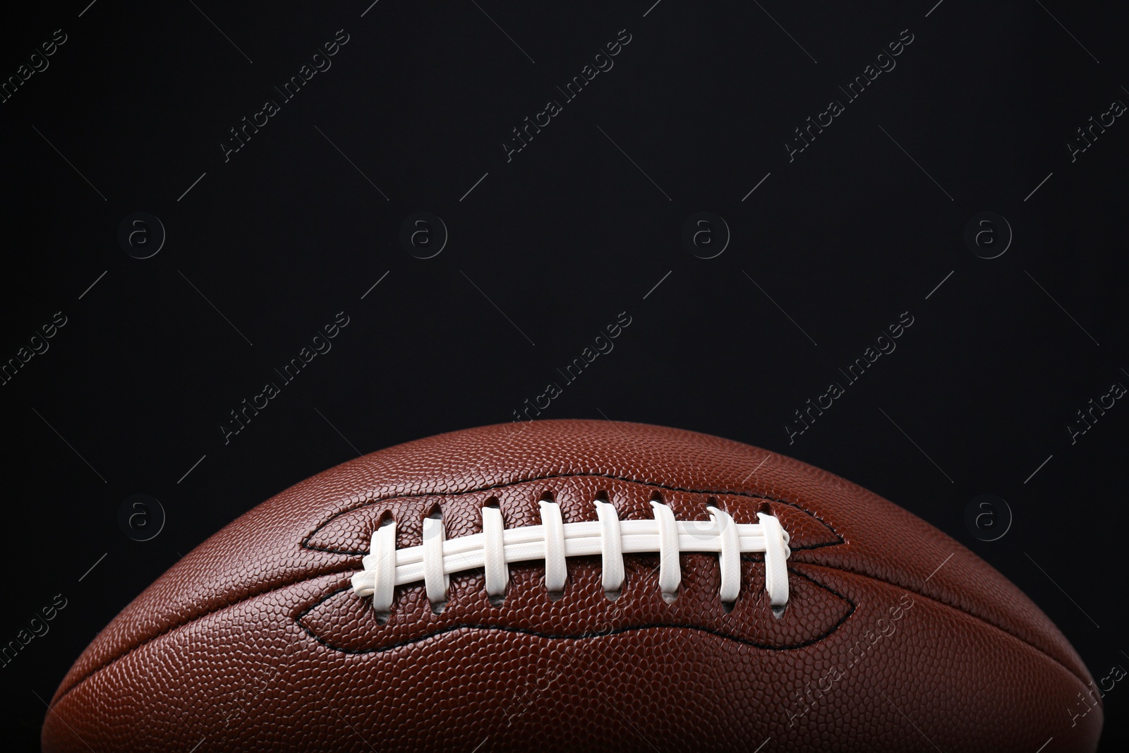 Photo of American football ball on black background, closeup. Space for text