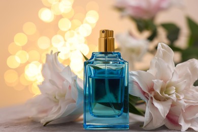 Photo of Bottle of perfume and beautiful lily flowers on table against beige background with blurred lights, closeup