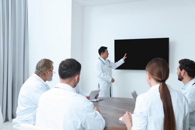Photo of Teamdoctors listening to speaker report near tv screen in meeting room. Medical conference