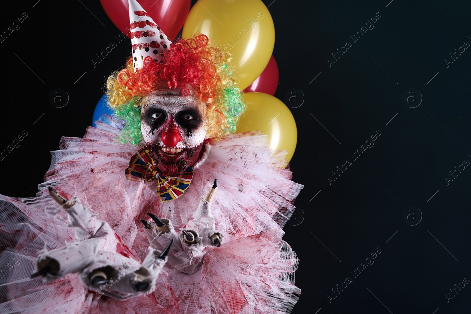 Photo of Terrifying clown with air balloons on black background, space for text. Halloween party costume