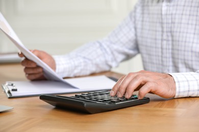 Photo of Professional accountant using calculator at wooden desk indoors, closeup