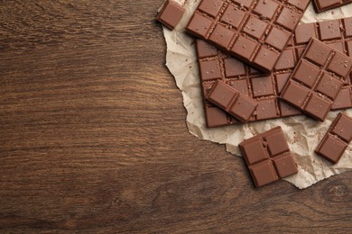 Photo of Pieces and crumbs of tasty chocolate bars on wooden table, top view. Space for text