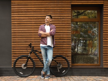 Handsome man with modern bicycle near building outdoors