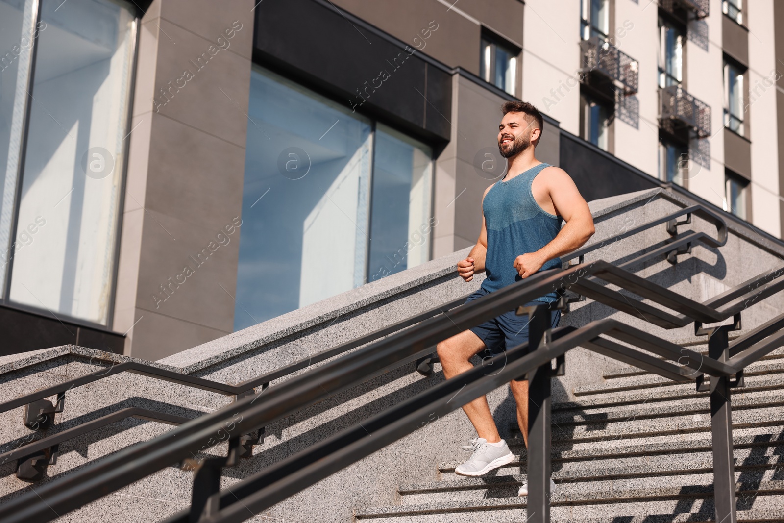 Photo of Happy man running down stairs outdoors on sunny day, low angle view. Space for text