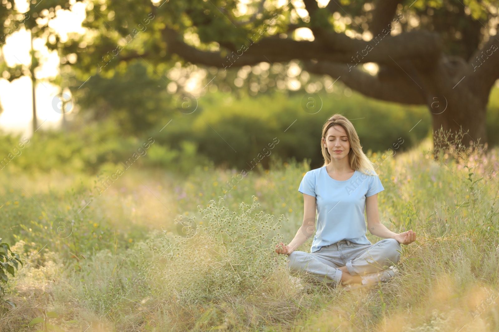 Photo of Young woman meditating on green grass in park, space for text