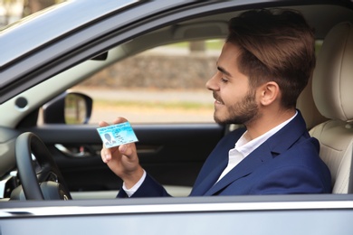 Photo of Young man holding driving license in car