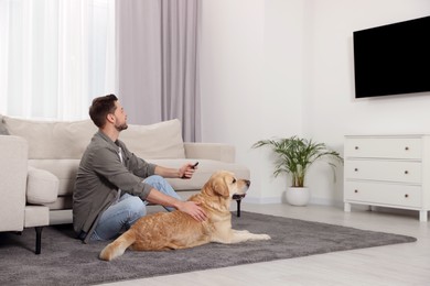 Photo of Man turning on TV near his cute Labrador Retriever at home. Space for text