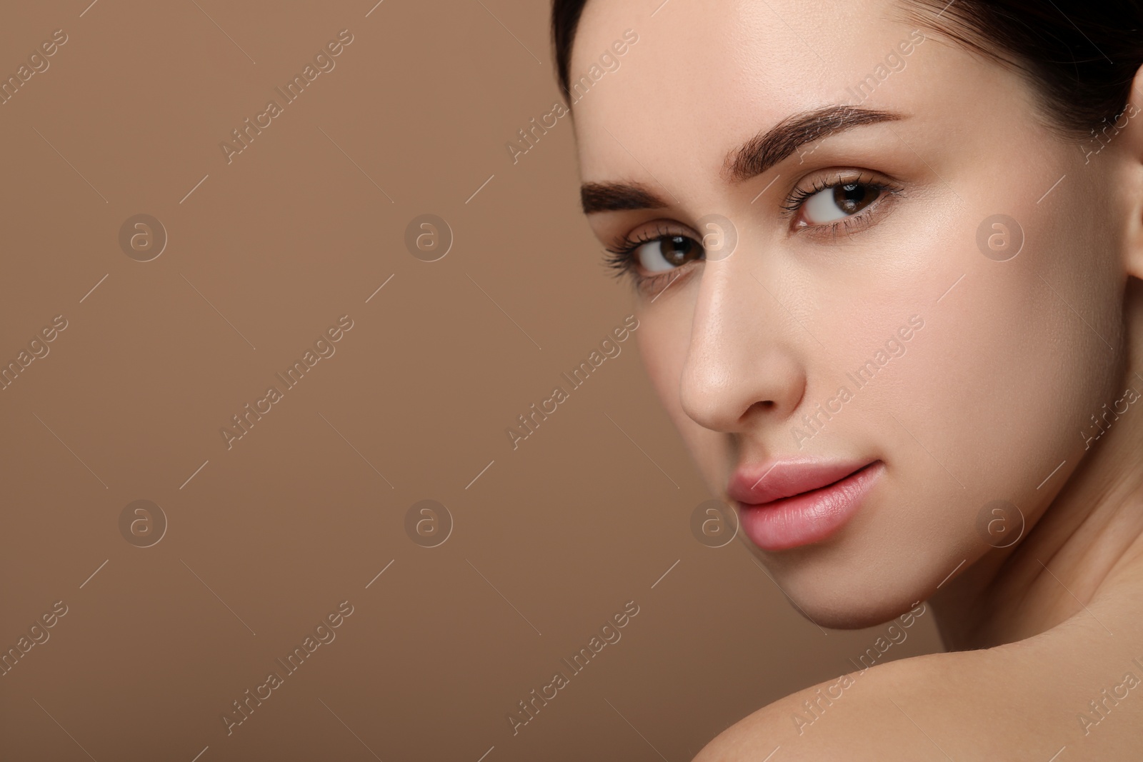 Photo of Beautiful young woman with healthy skin on brown background, closeup. Space for text