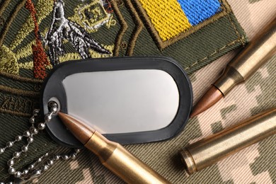 Photo of Bullets, military ID tag and Ukrainian patch on pixel camouflage, flat lay