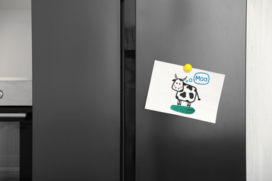 Photo of Modern refrigerator with child's drawing and magnet in kitchen