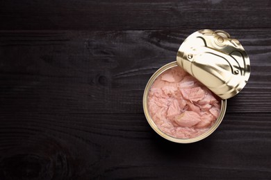 Photo of Tin can with canned tuna on black wooden table, top view. Space for text