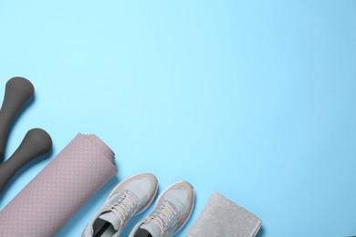 Exercise mat, dumbbells, towel and shoes on light blue background, flat lay. Space for text