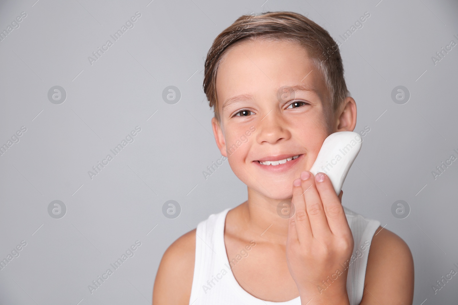 Photo of Cute little boy with soap bar on gray background