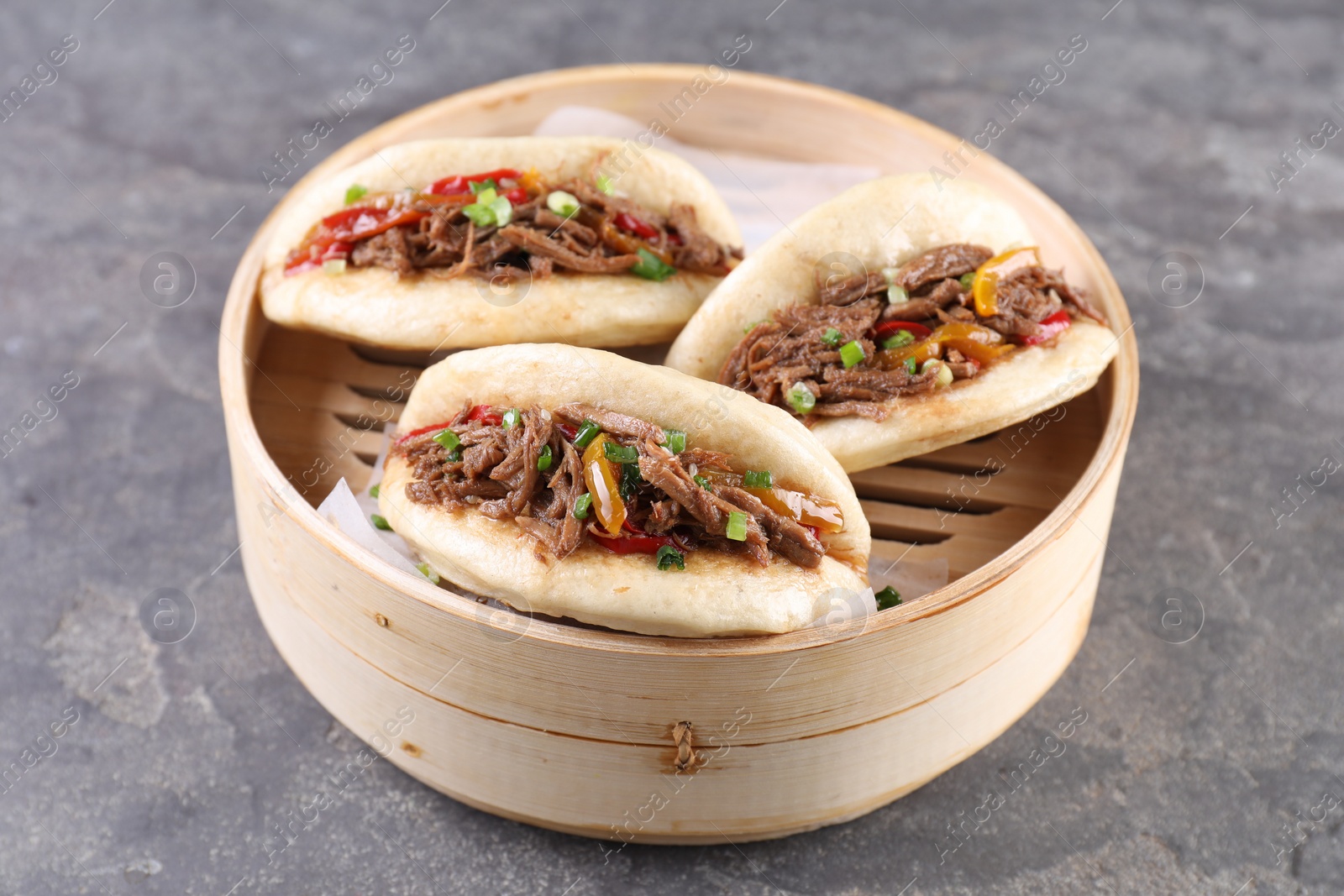 Photo of Delicious gua bao in bamboo steamer on grey table