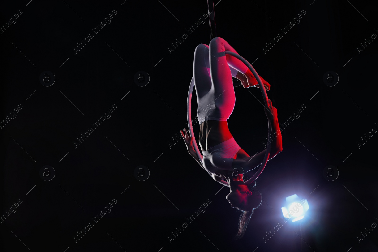 Photo of Young woman performing acrobatic element on aerial ring against dark background. Space for text