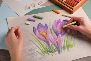 Photo of Woman drawing beautiful crocus flowers with soft pastel at wooden table, closeup