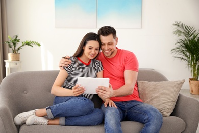 Photo of Happy couple with tablet sitting on couch at home