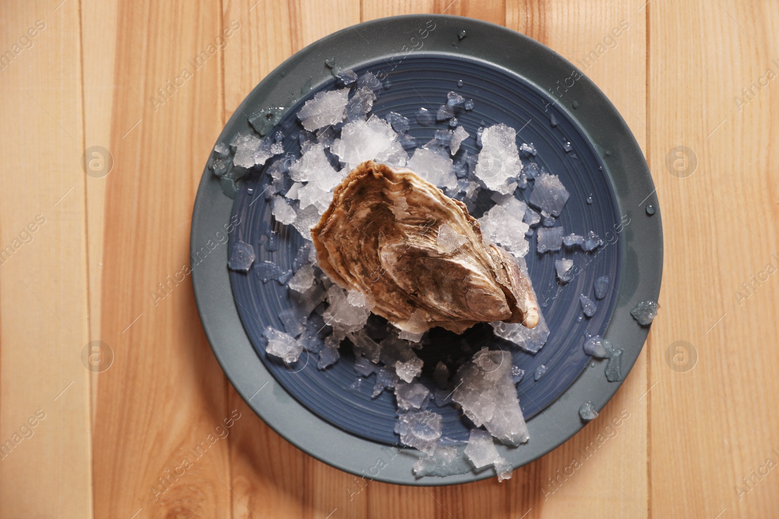 Photo of Fresh oyster with ice on wooden table, top view