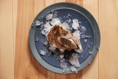 Photo of Fresh oyster with ice on wooden table, top view