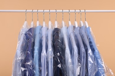 Photo of Dry-cleaning service. Many different clothes in plastic bags hanging on rack against beige background