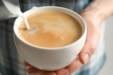 Woman pouring milk into cup of hot coffee, closeup