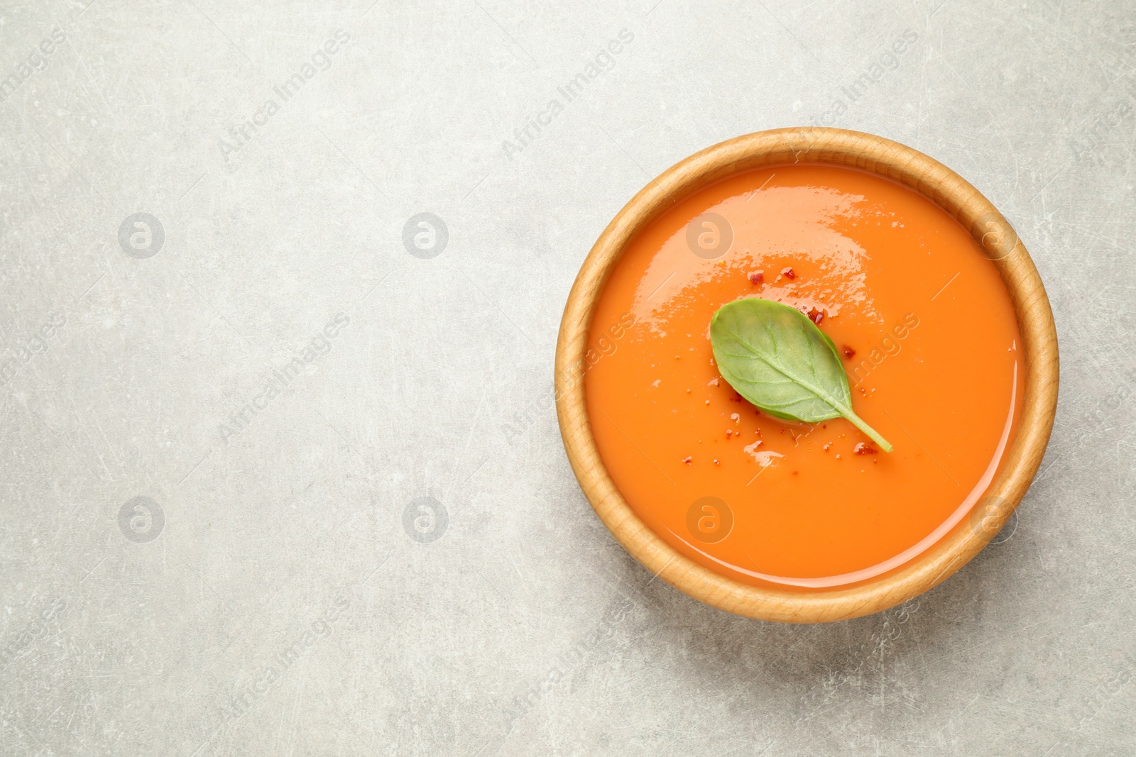 Photo of Tasty creamy pumpkin soup with basil in bowl on light grey table, top view. Space for text