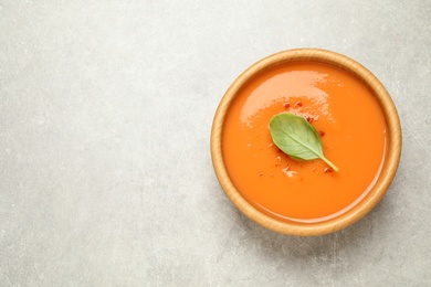 Photo of Tasty creamy pumpkin soup with basil in bowl on light grey table, top view. Space for text