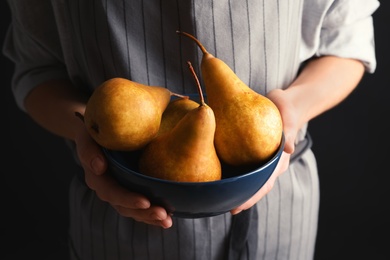 Photo of Woman holding bowl with ripe pears on black background, closeup