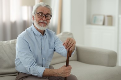 Portrait of grandpa with glasses and walking cane on sofa indoors