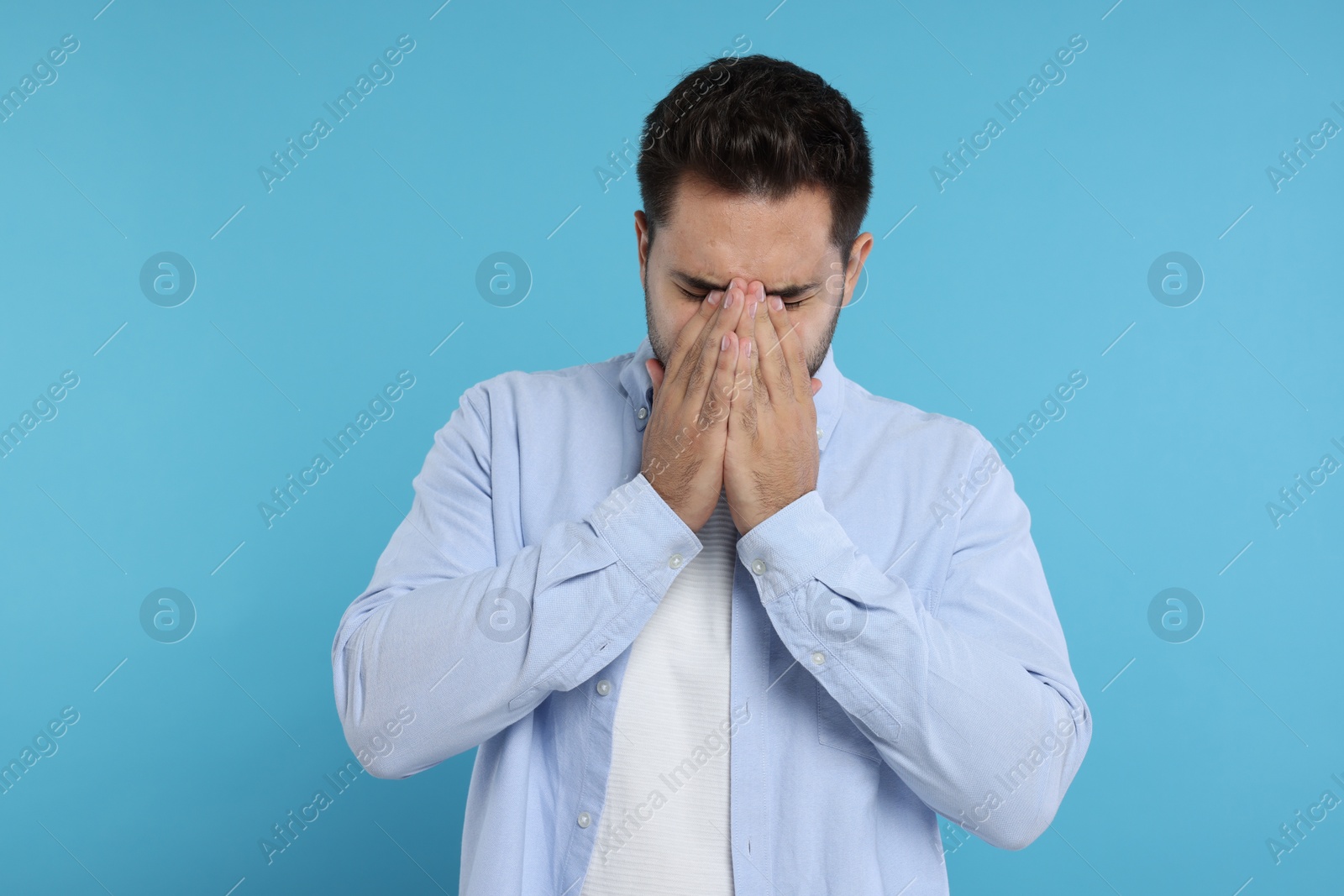 Photo of Resentful man covering face with hands on light blue background