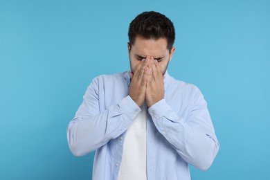 Resentful man covering face with hands on light blue background