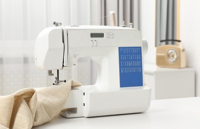 Photo of Sewing machine and fabric on white table in workshop