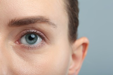 Woman with beautiful natural eyelashes on grey background, closeup