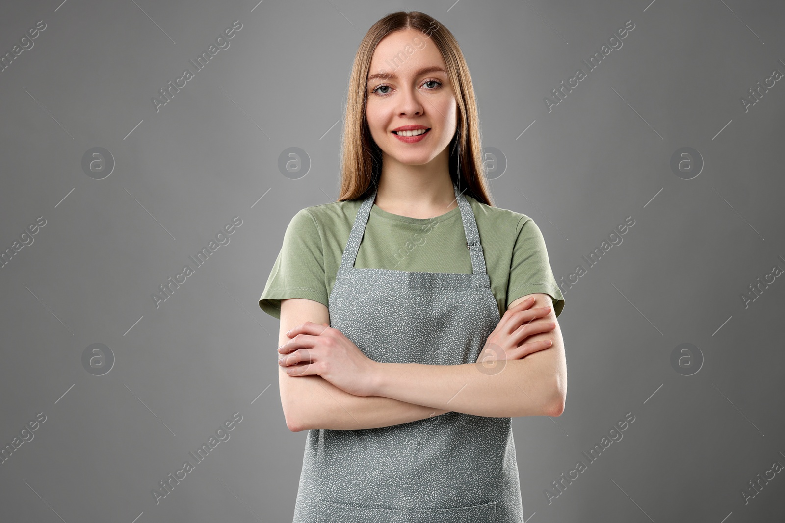 Photo of Beautiful young woman wearing kitchen apron on grey background. Mockup for design