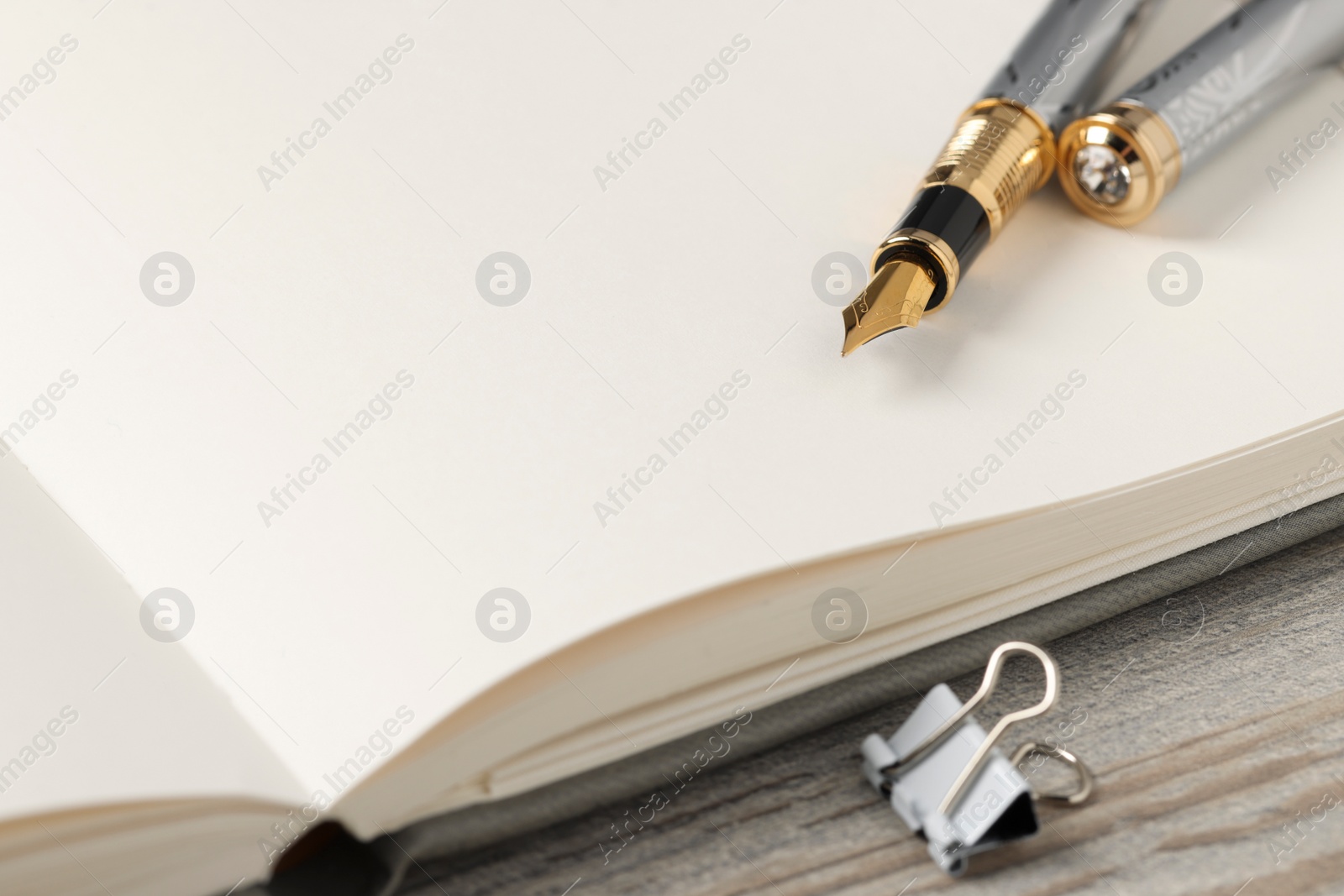 Photo of Fountain pen, notebook and binder clip on wooden table, closeup