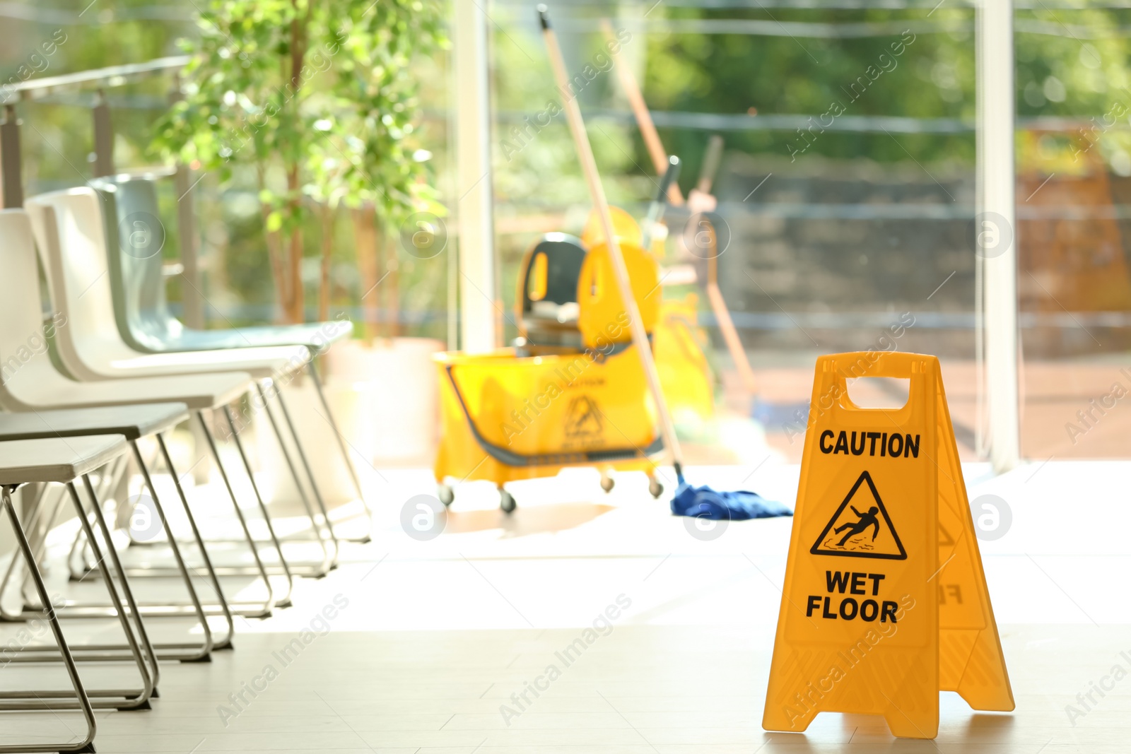 Photo of Safety sign with phrase Caution wet floor and blurred mop bucket on background. Cleaning service