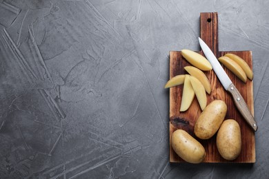 Photo of Raw potatoes, knife and wooden board on grey table, top view. Space for text