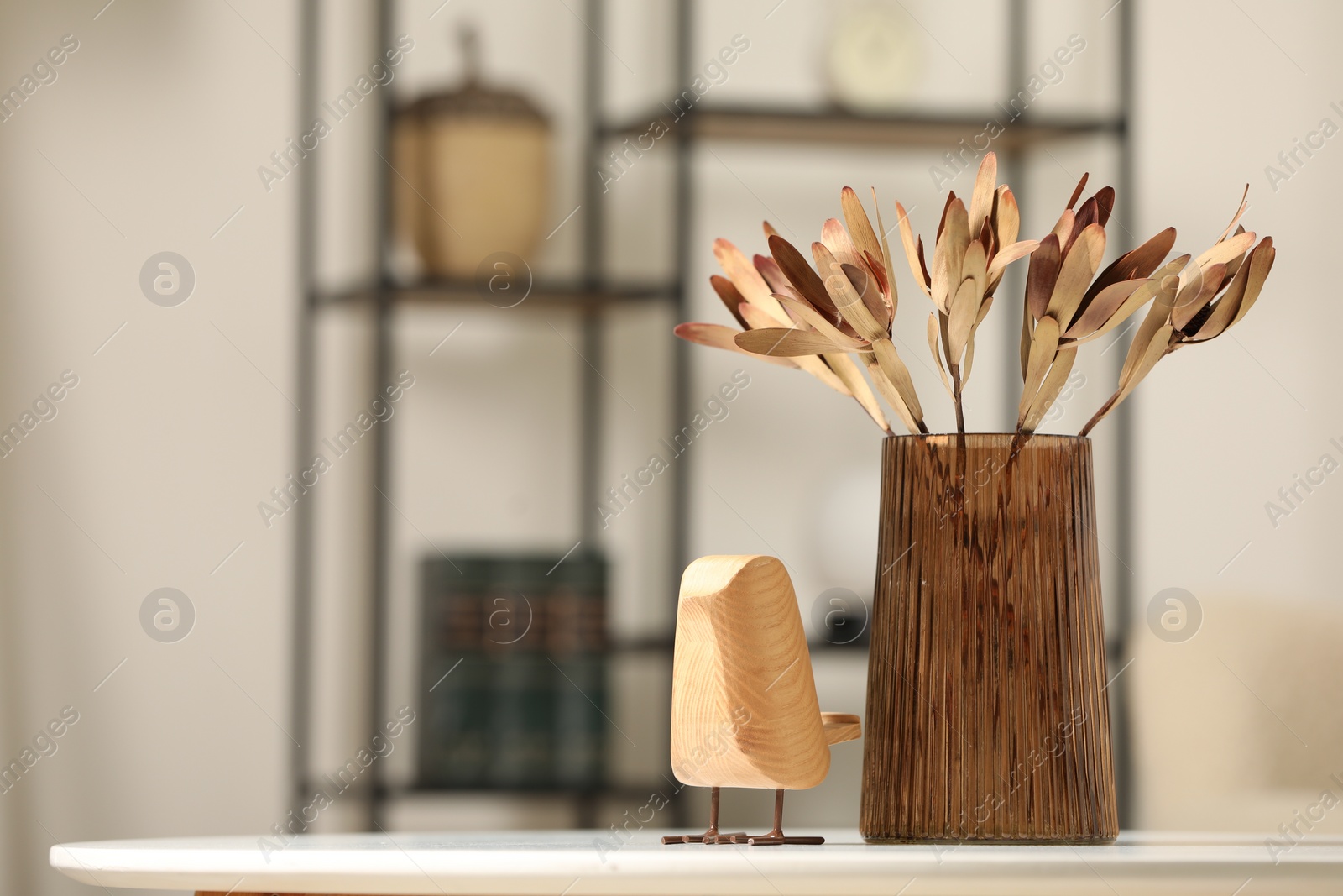 Photo of Vase with beautiful dried leucadendron plants and wooden bird on white table in room, space for text